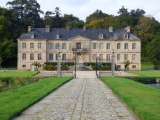 A large building with a walkway leading to it is surrounded by grass and trees.