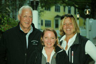 A man and two women are posing for a picture in front of a yellow house.