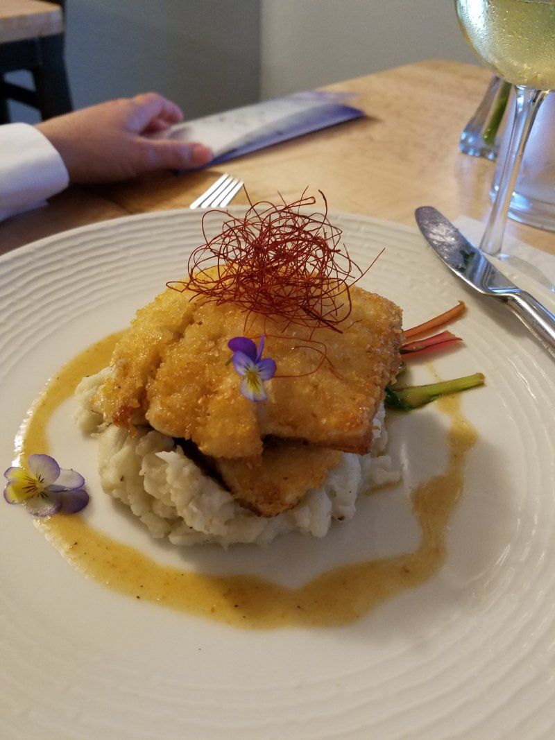 A person is sitting at a table with a plate of food and a glass of wine.