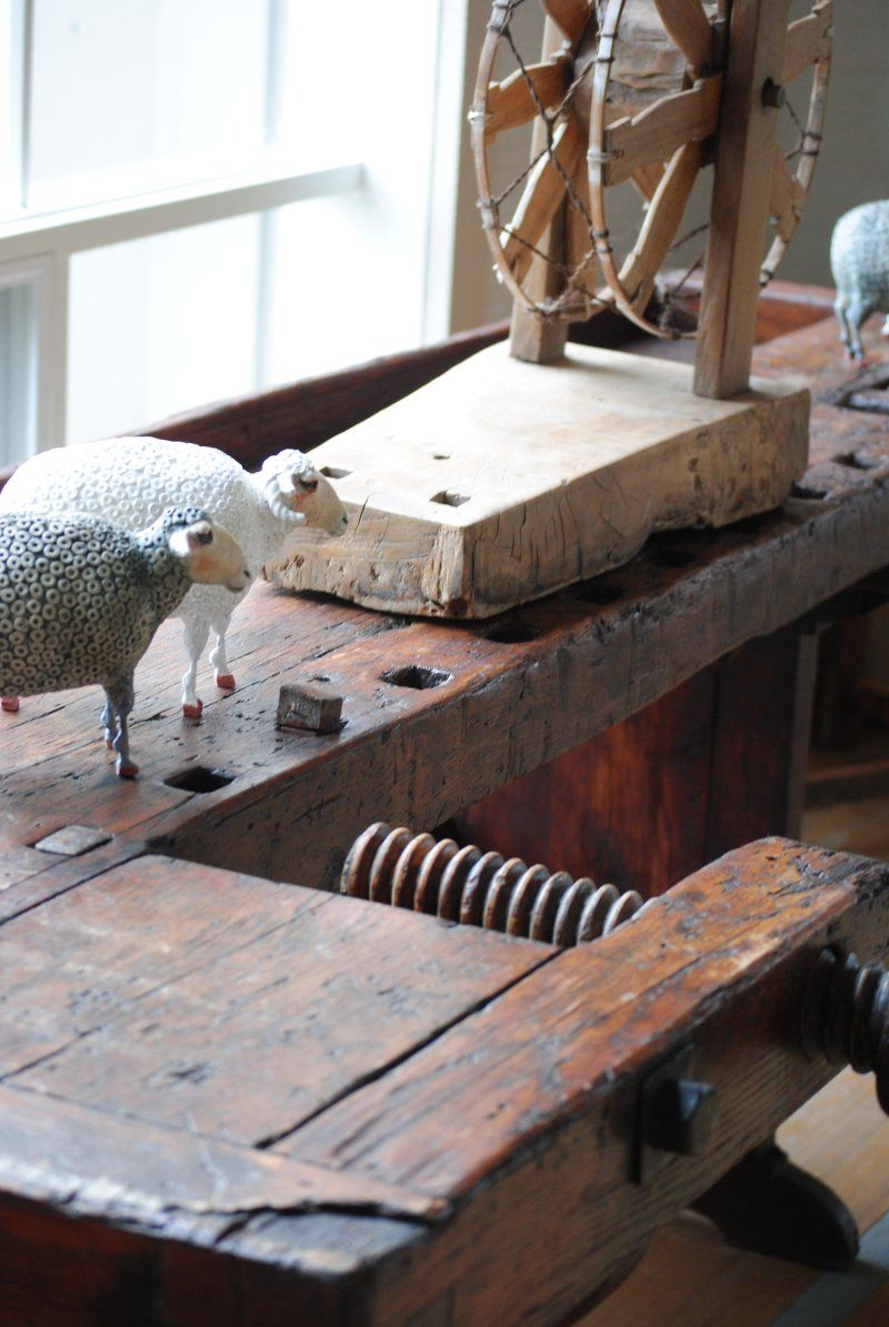 Two sheep are standing on a wooden table next to a spinning wheel