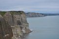 A cliff overlooking the ocean with a cliff in the foreground and a body of water in the background.