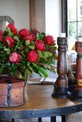 A vase of red roses is sitting on a wooden table next to candles.