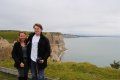 A man and a woman are standing on top of a cliff overlooking the ocean.