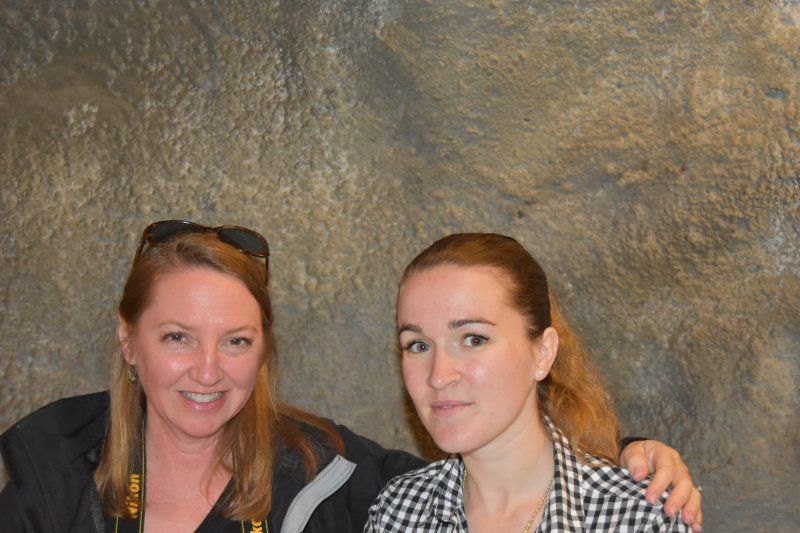 Two women are posing for a picture in front of a rock wall.