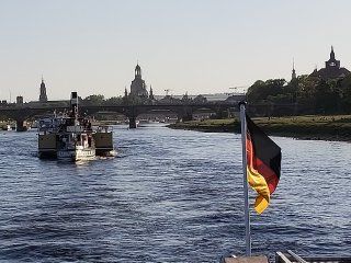 A boat is going down a river with a german flag in the foreground