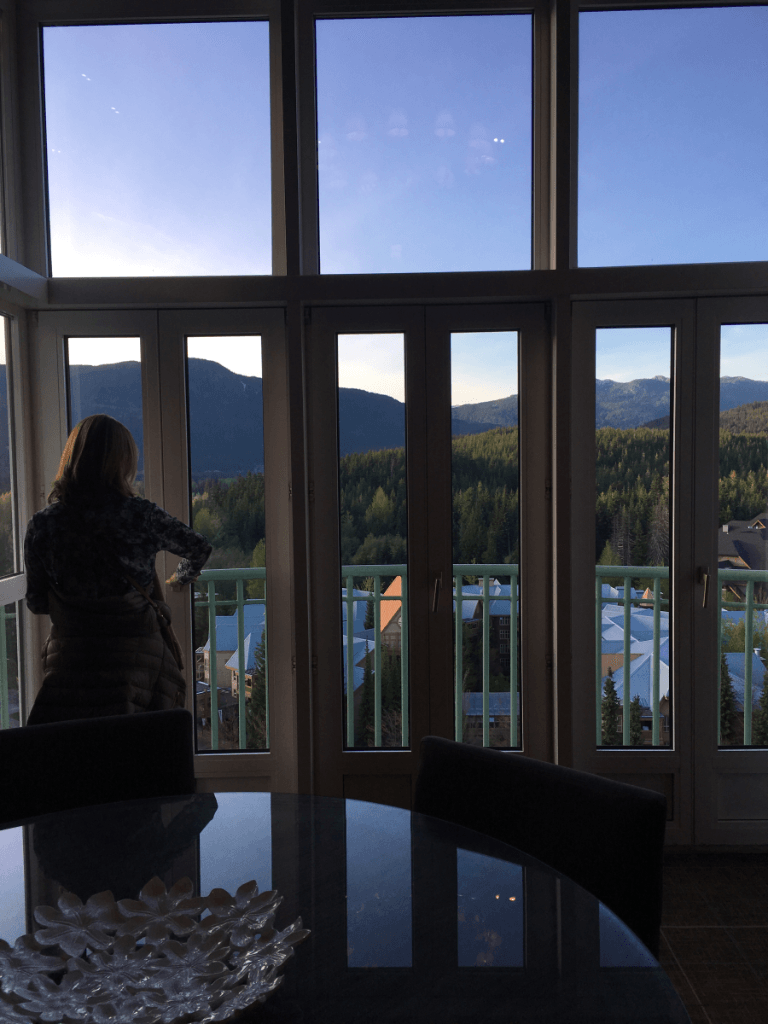 A woman stands in front of a large window looking out