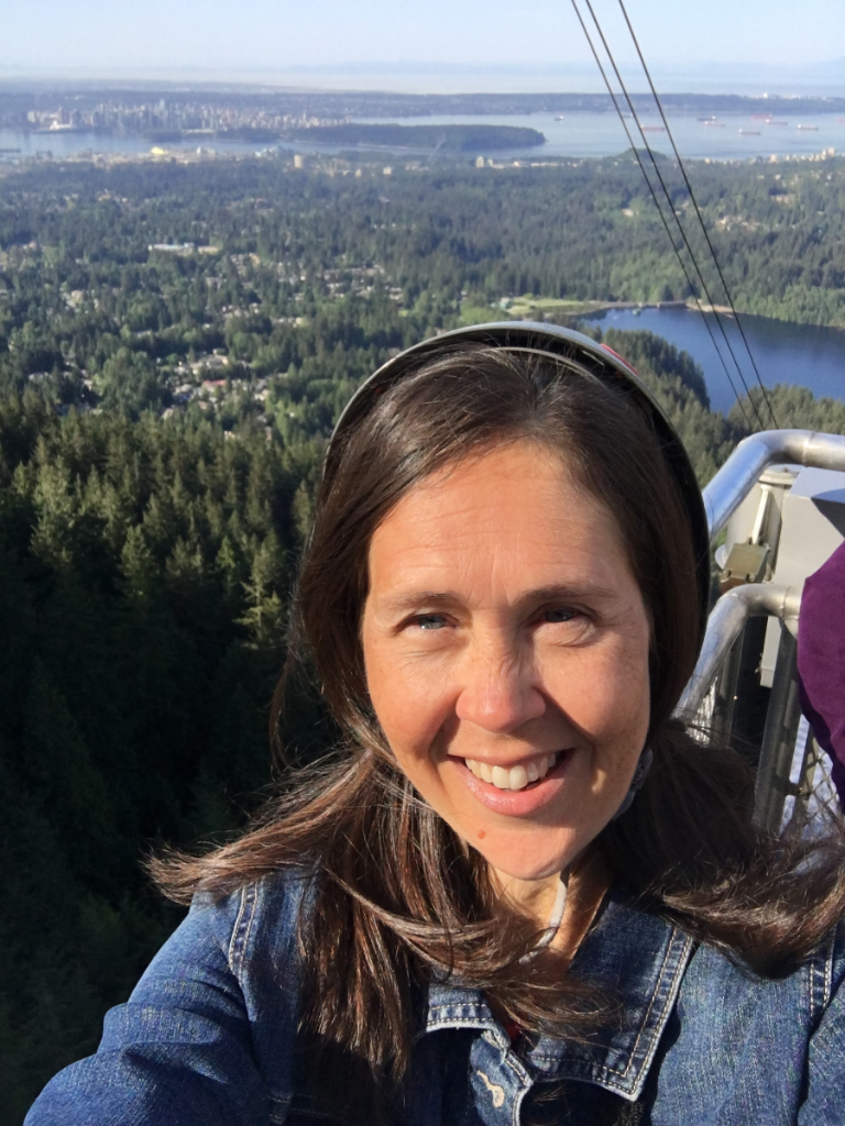 A woman is smiling while taking a selfie with a view of a forest.