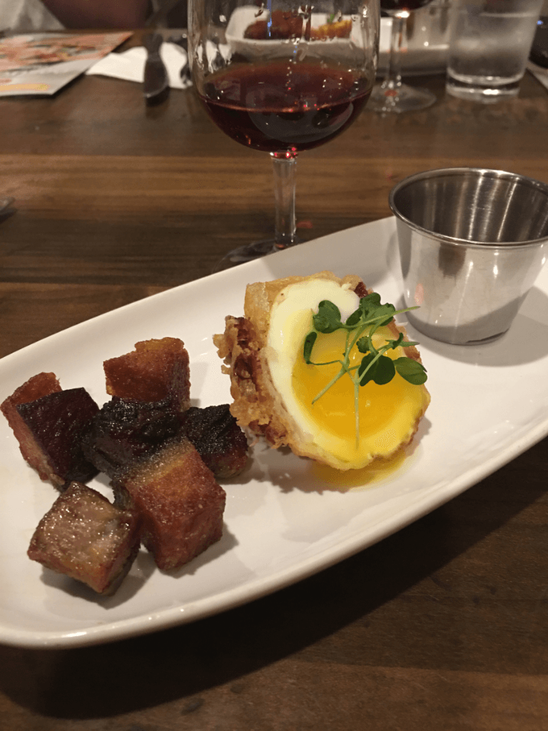 A plate of food with a glass of wine in the background