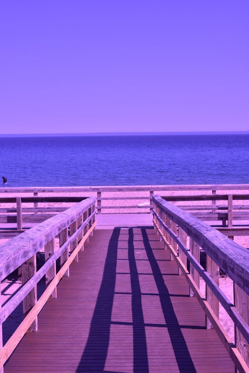 A wooden walkway leading to the ocean with a purple sky