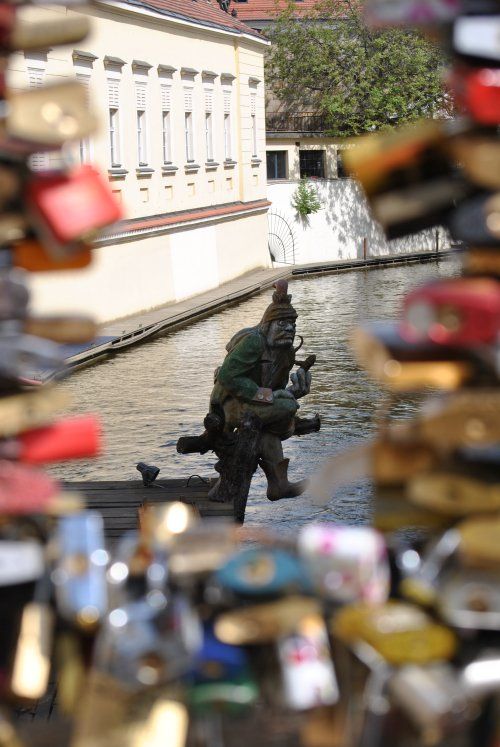 A statue of a man standing next to a river surrounded by love locks.