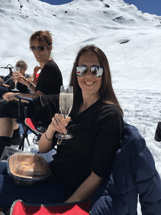 A woman is sitting in the snow holding a glass of champagne.