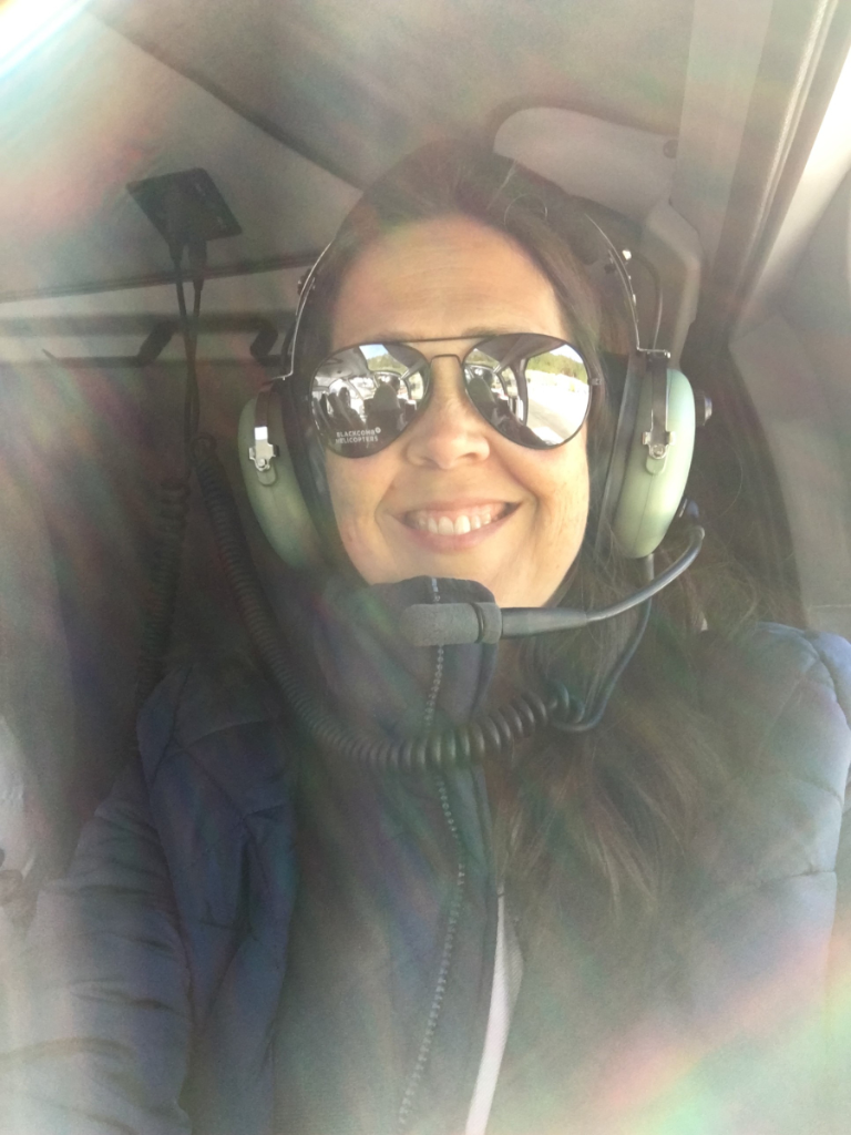 A woman wearing sunglasses and headphones is sitting in a helicopter.