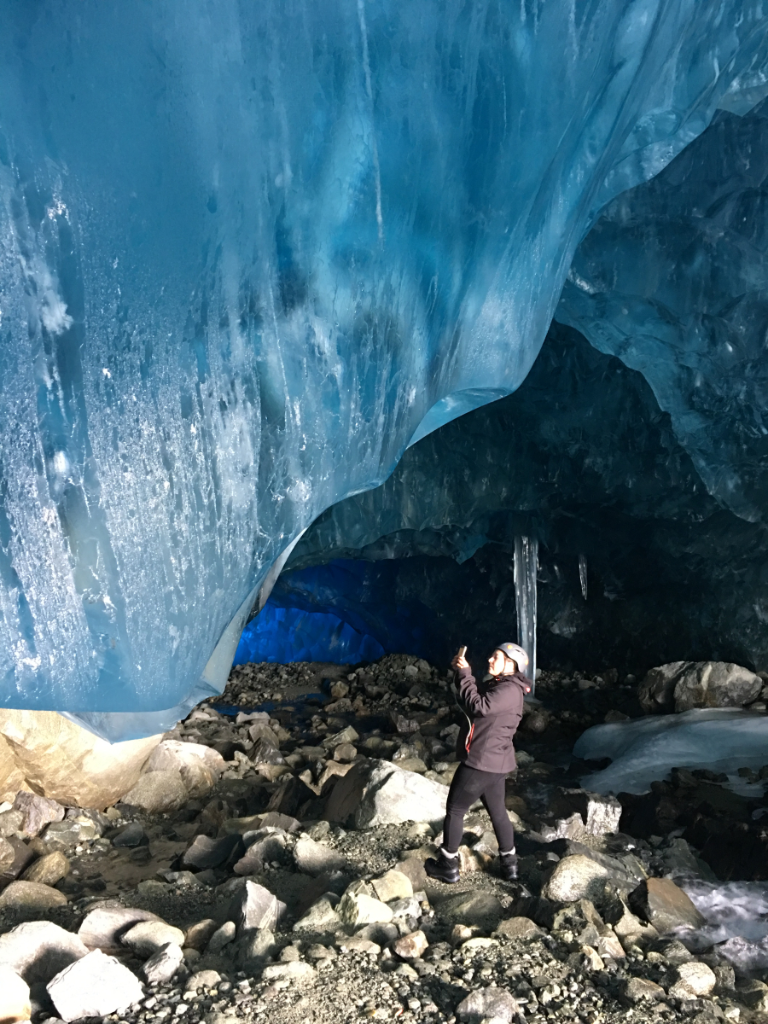A person is standing inside of an ice cave taking a picture.