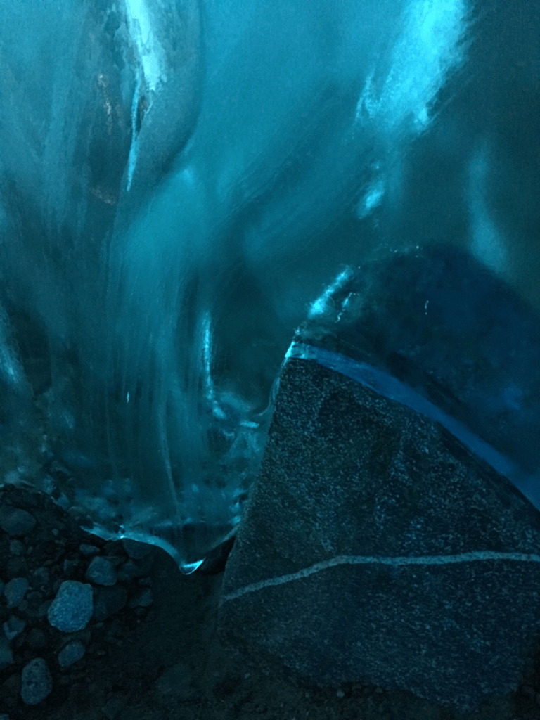 A close up of a blue ice cave with a rock in the foreground.