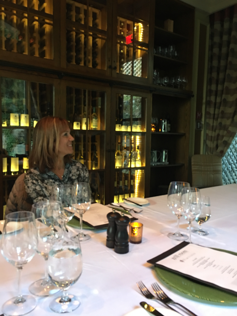 A woman sits at a table with wine glasses and a menu