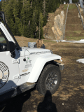 A white jeep is parked on the side of a dirt road.