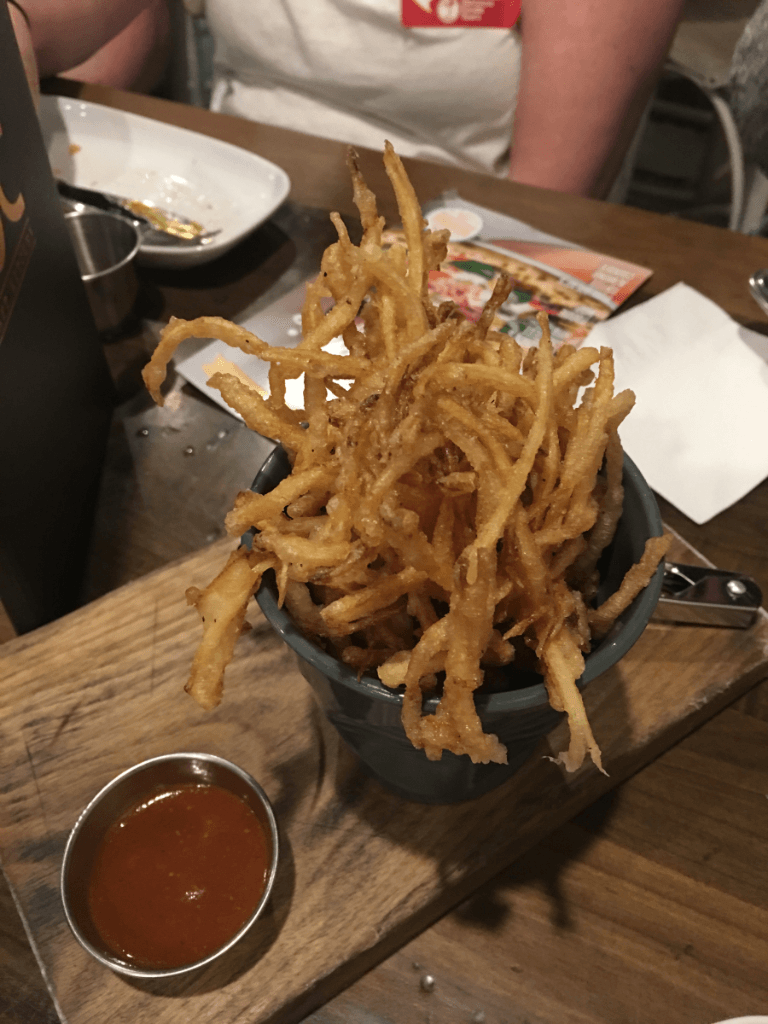 A bowl of french fries with ketchup on a wooden cutting board.