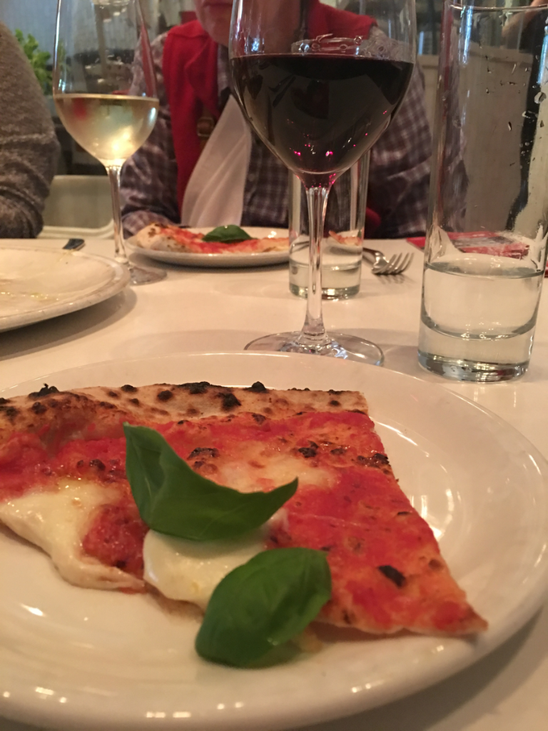 A slice of pizza on a plate next to a glass of wine
