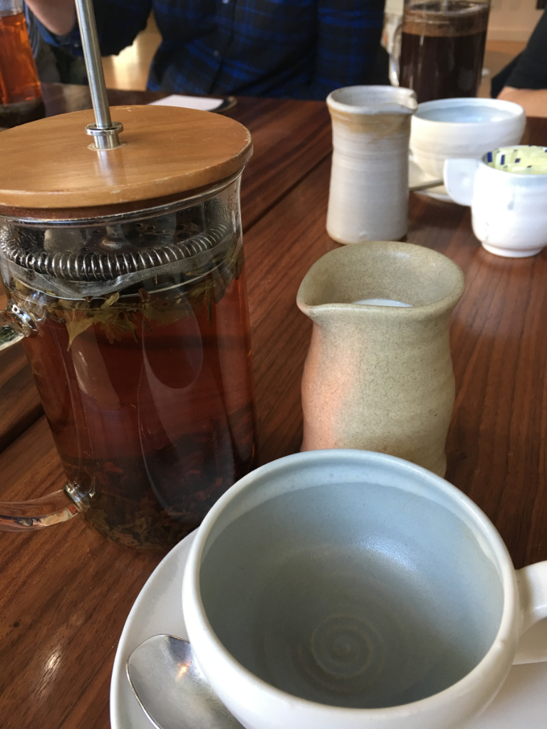 A french press filled with tea sits on a table next to a cup and saucer.