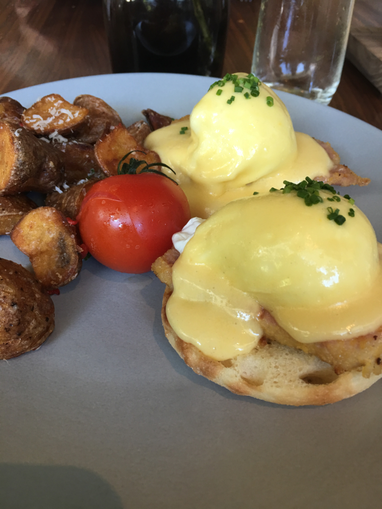 A plate of food with eggs benedict and potatoes on a table.
