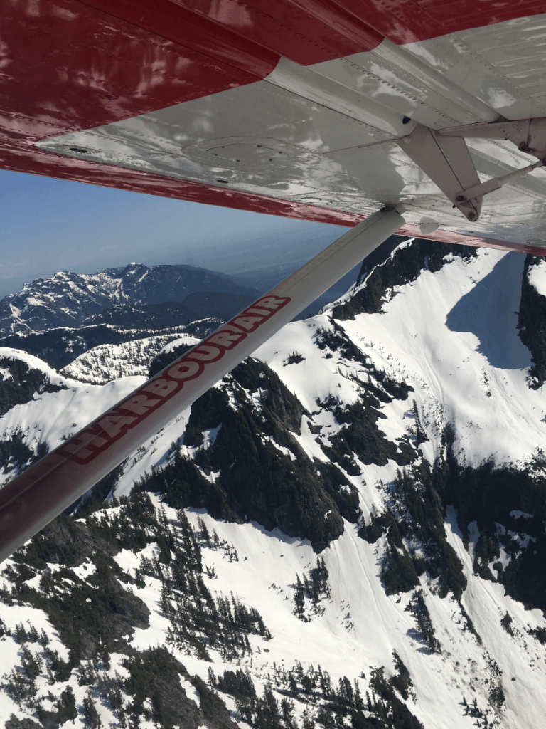 A red and white plane is flying over snow covered mountains