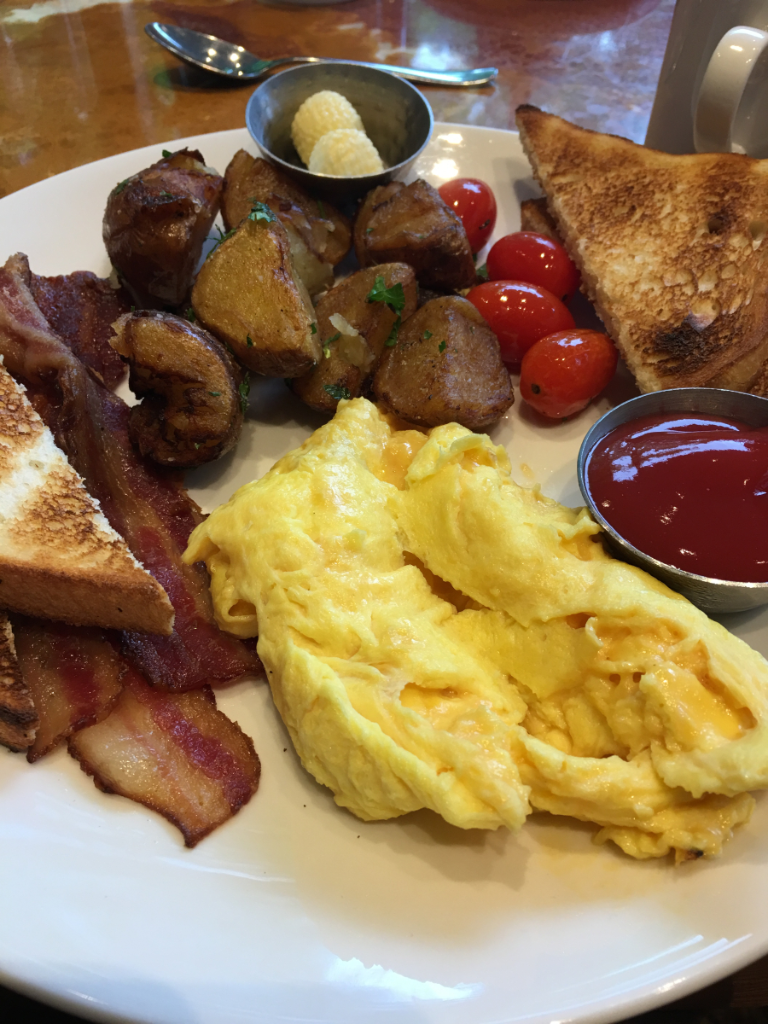 A white plate topped with eggs , bacon , potatoes , tomatoes and toast.