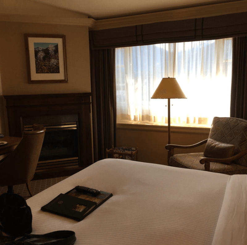 A hotel room with a bed a chair a lamp and a fireplace