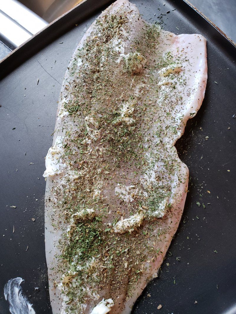 A piece of fish is sitting on a pan with seasoning on it.