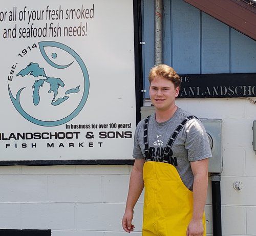A man in yellow overalls stands in front of a sign that says