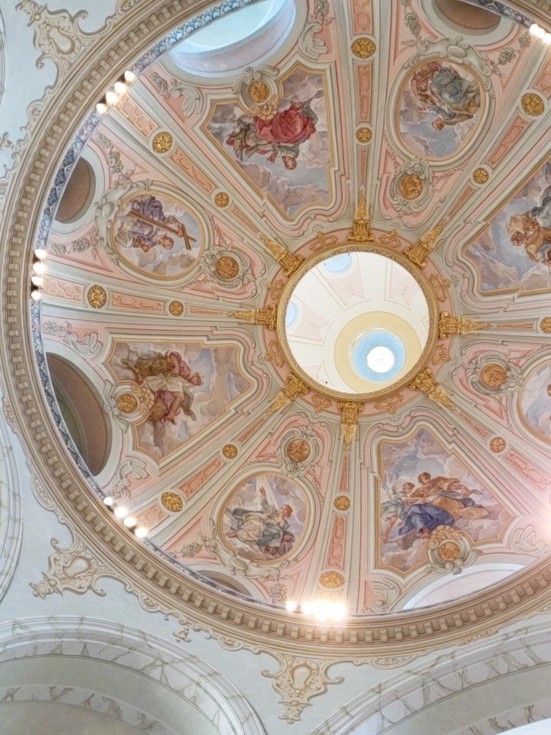 Looking up at the ceiling of a church with paintings on it.