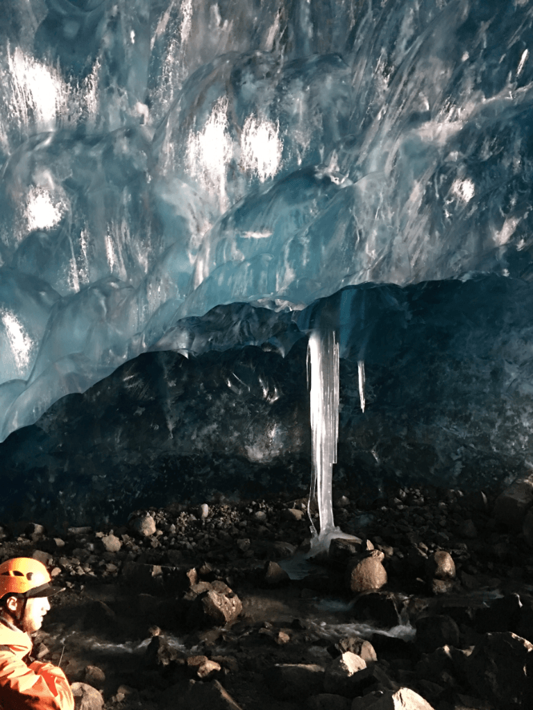 A person is standing in an ice cave with icicles hanging from the ceiling.