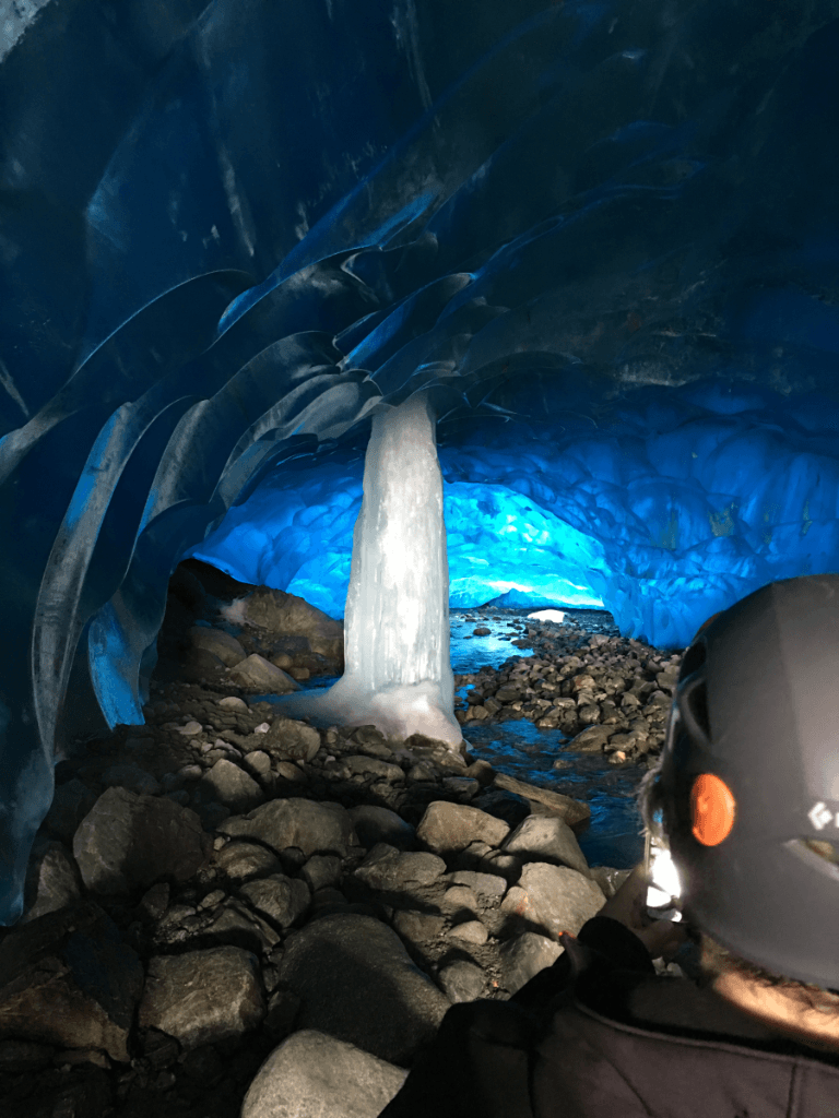 A person wearing a helmet is standing inside of an ice cave.