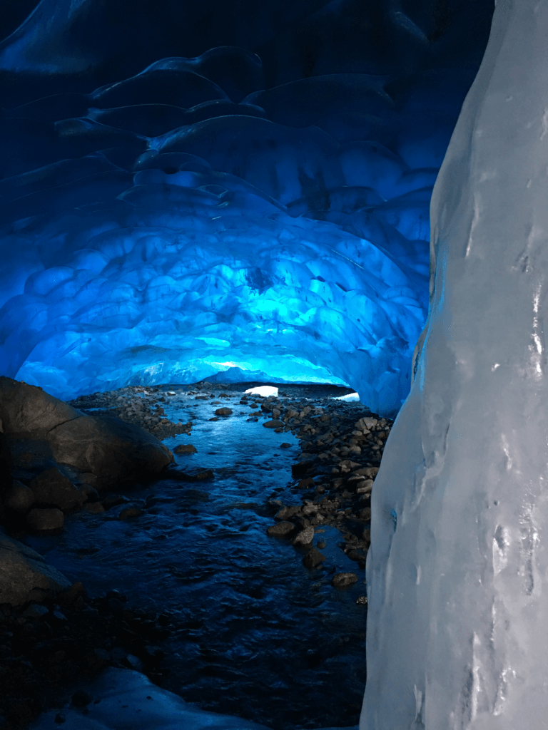 A large ice cave with a river coming out of it.