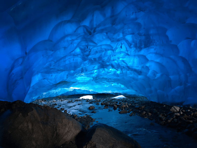 A blue ice cave filled with water and rocks.