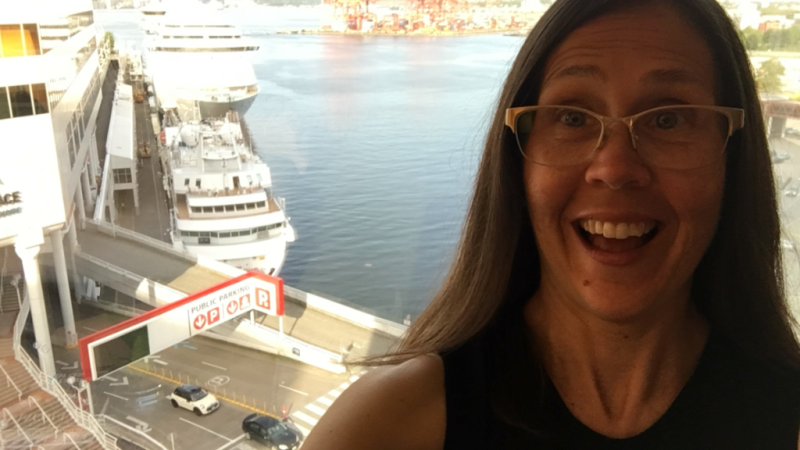 A woman wearing glasses is smiling in front of a large ship in the water.