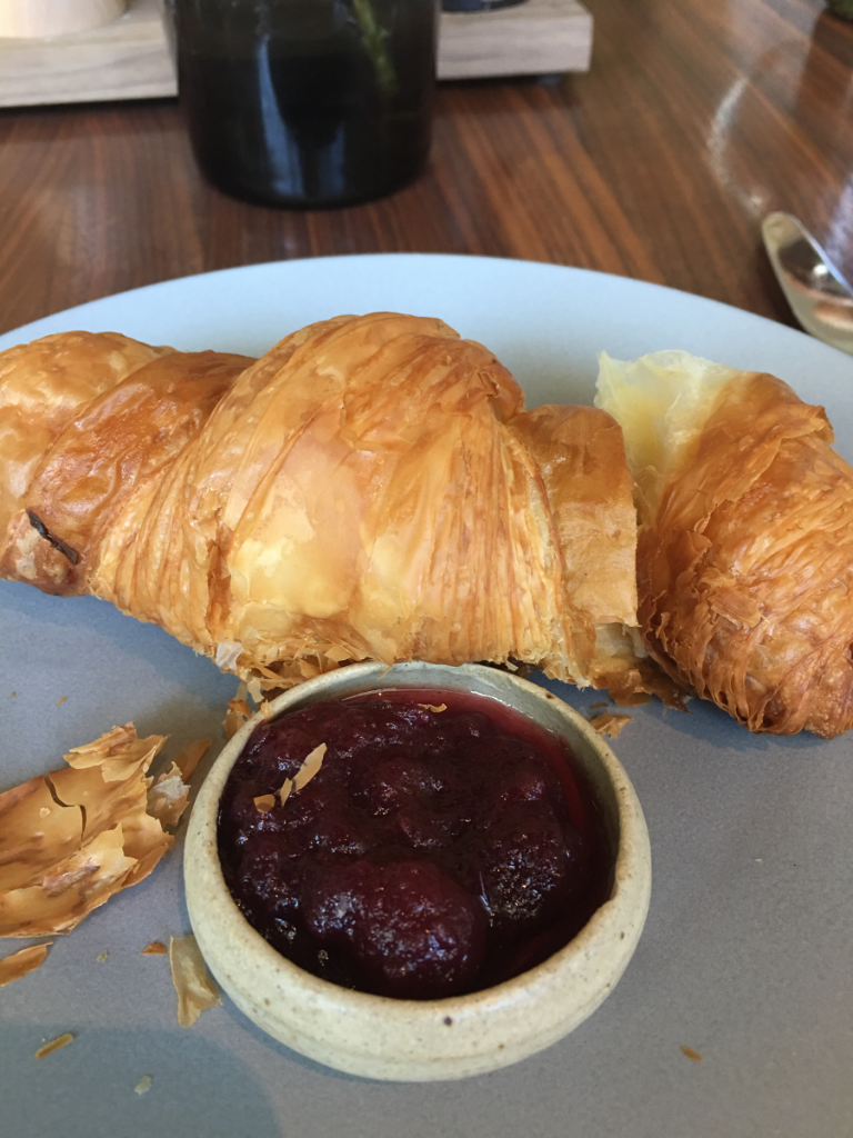A close up of a plate of food with a croissant and a bowl of jam.