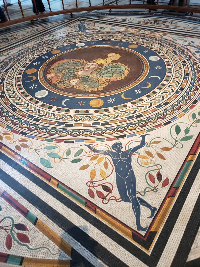A colorful mosaic floor with a statue of a man in the center.