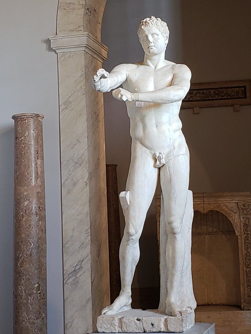 A statue of a man without a shirt is standing in a museum.