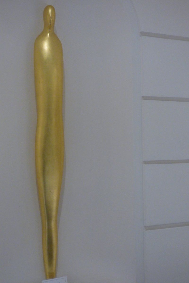 A gold statue of a man is hanging on a white wall.