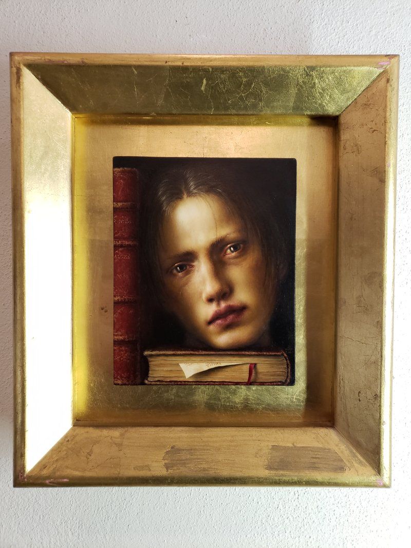 A framed painting of a woman 's face on top of a book