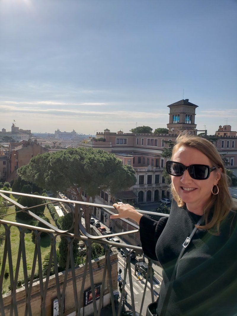 A woman wearing sunglasses is standing on a balcony overlooking a city.