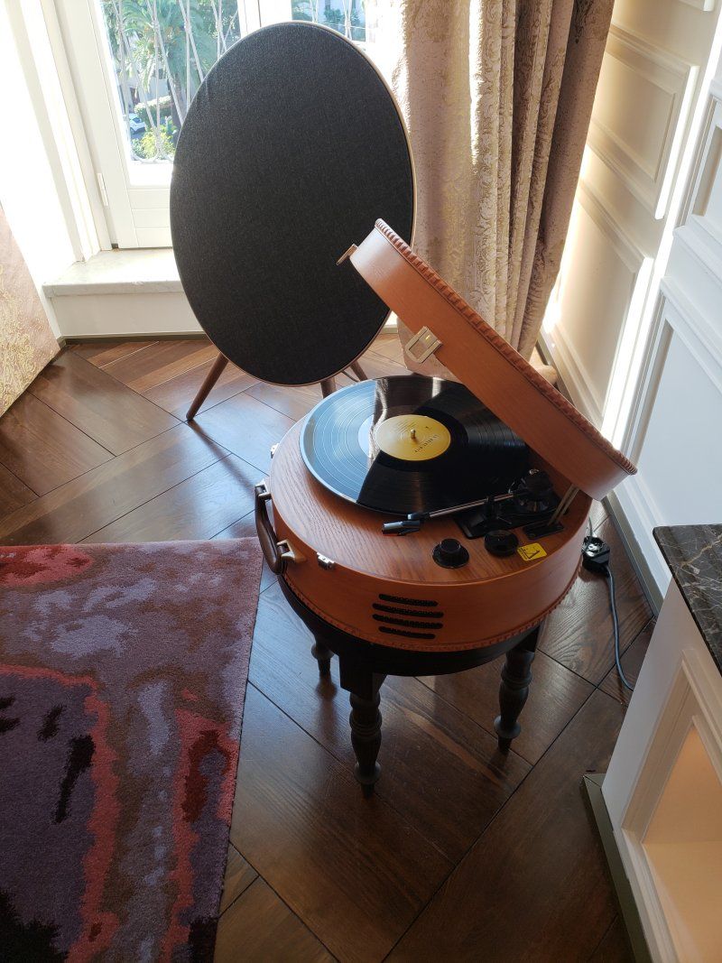 A record player is sitting on a wooden floor next to a window