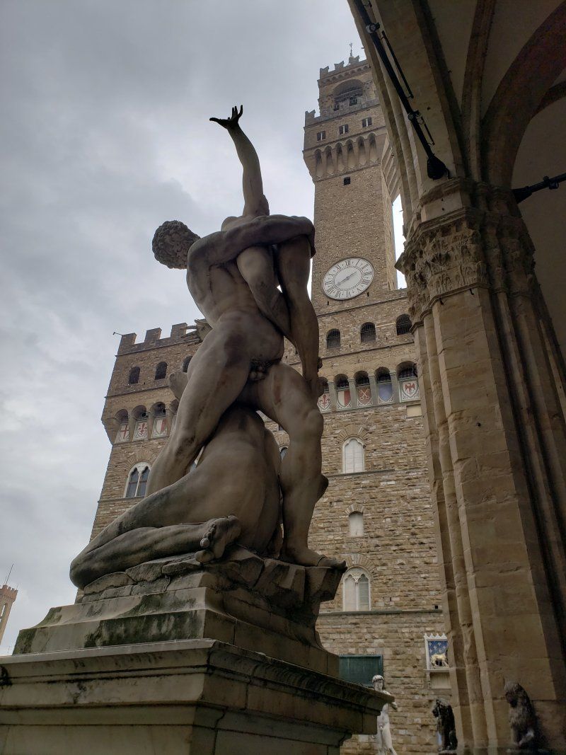 A statue of a man carrying a dog in front of a clock tower.