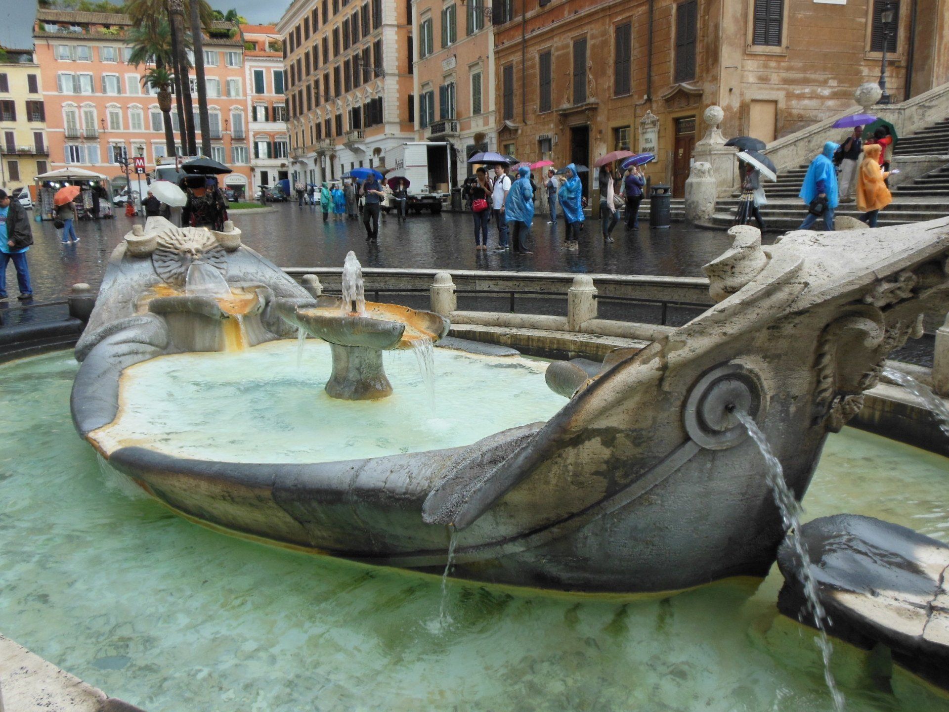 A group of people are standing around a fountain in the rain.