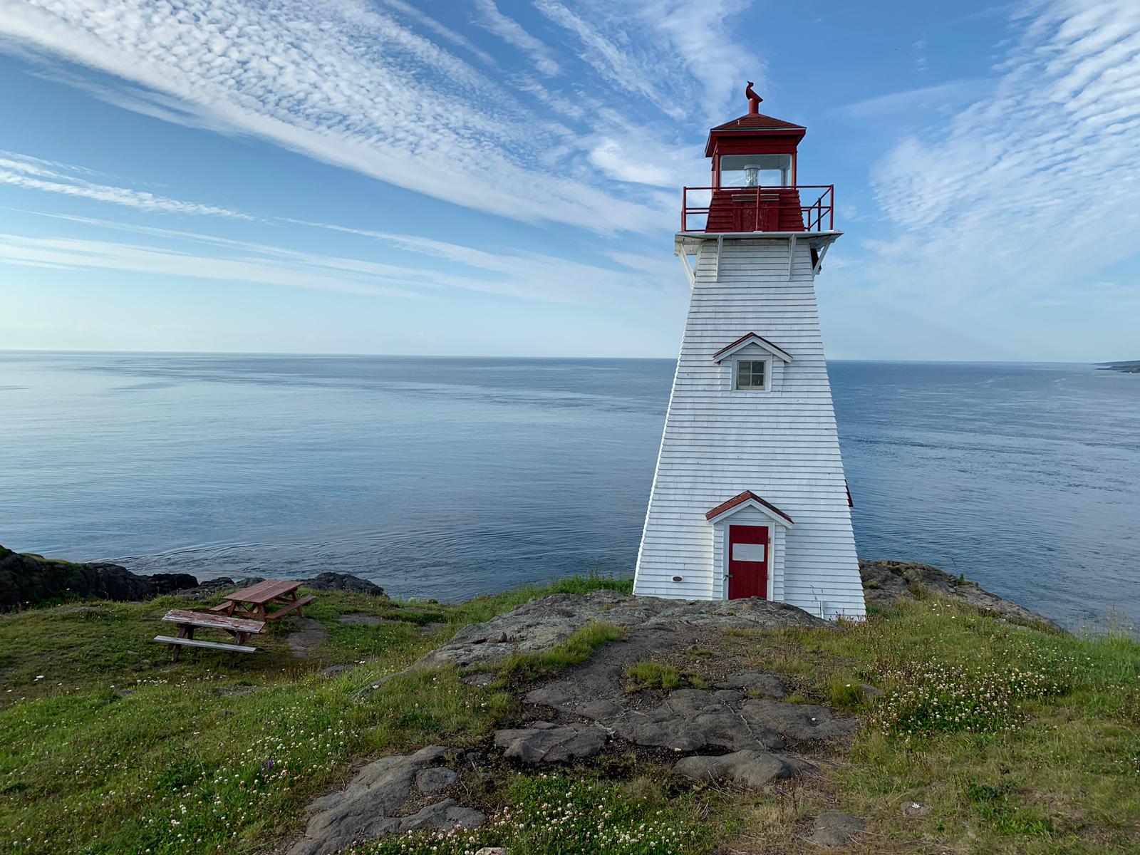A lighthouse is sitting on top of a grassy hill overlooking the ocean.