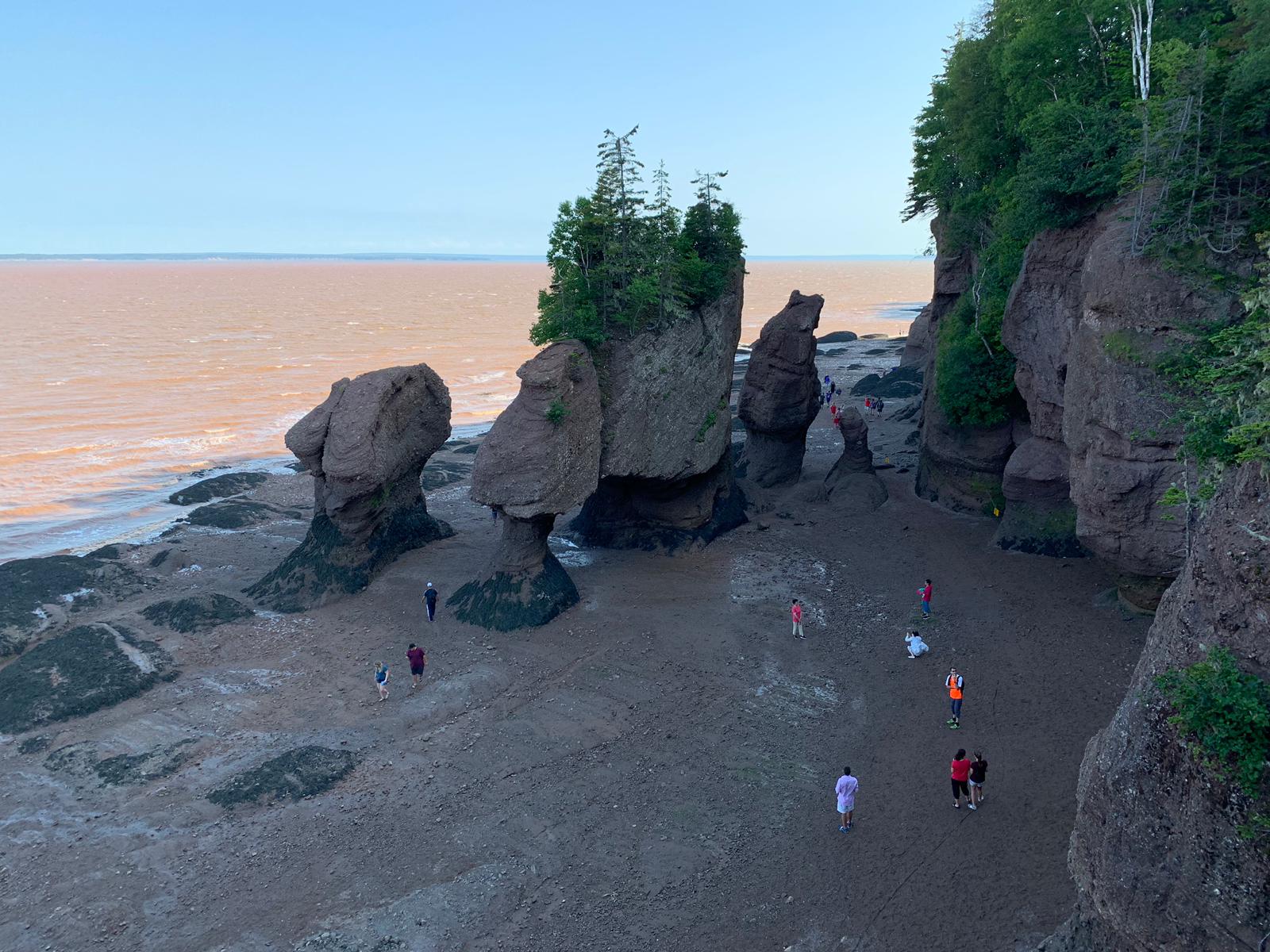 A group of people are standing on a beach next to a large rock formation.