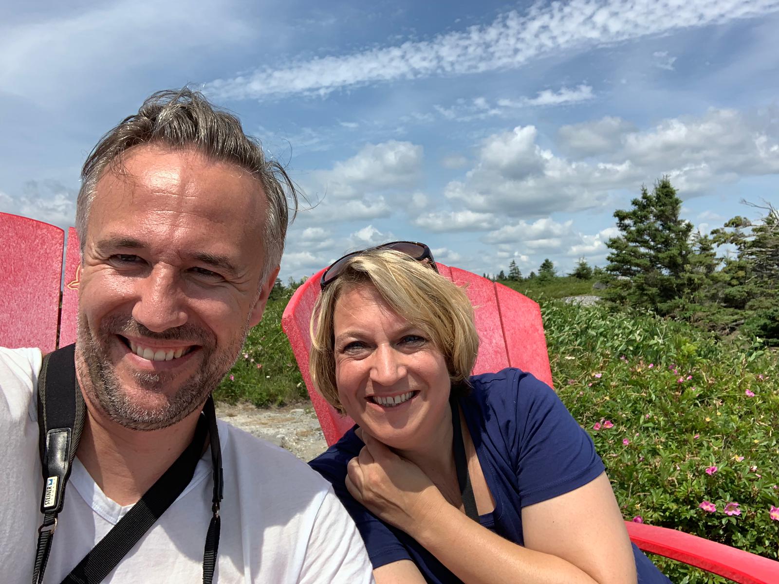A man and a woman are posing for a picture while sitting in red chairs.