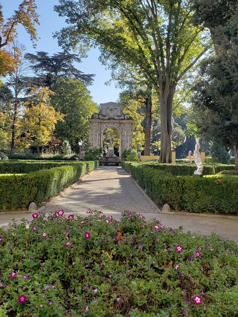 There is a statue in the middle of the park surrounded by trees and bushes.