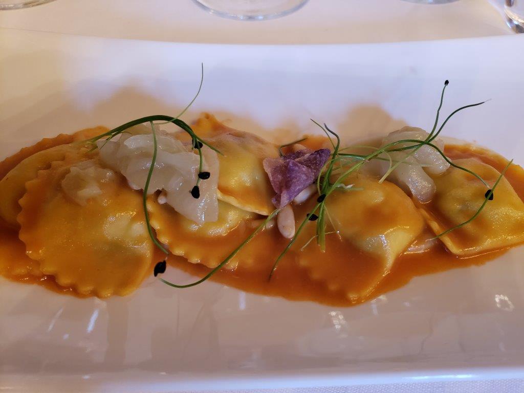 A white plate topped with ravioli and sauce on a table.