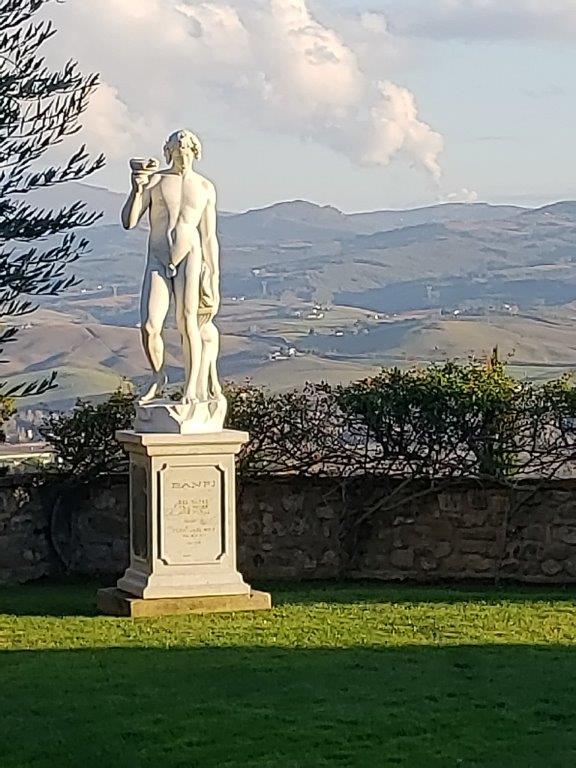 A statue of a man standing on a pedestal in a field with mountains in the background.
